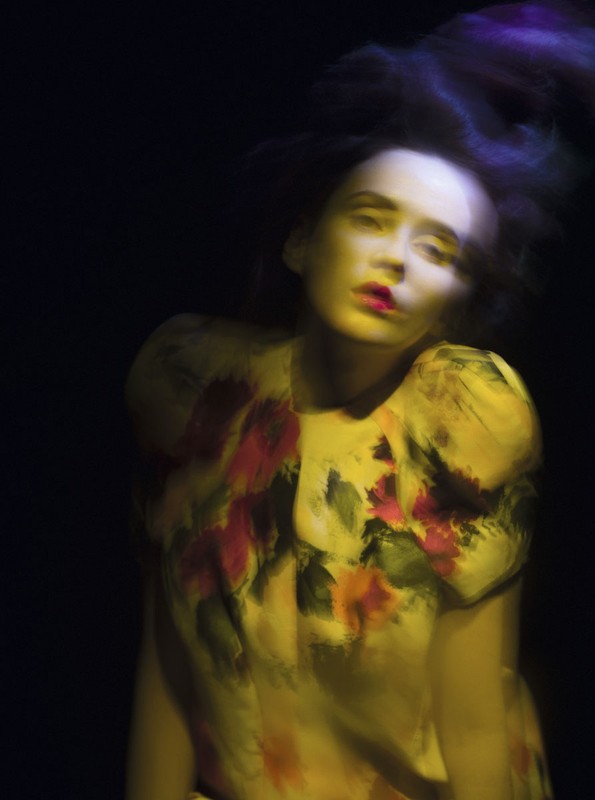 Woman in yellow floral dress with smeared colors and motion blur against a dark background in a fashion or beauty context.