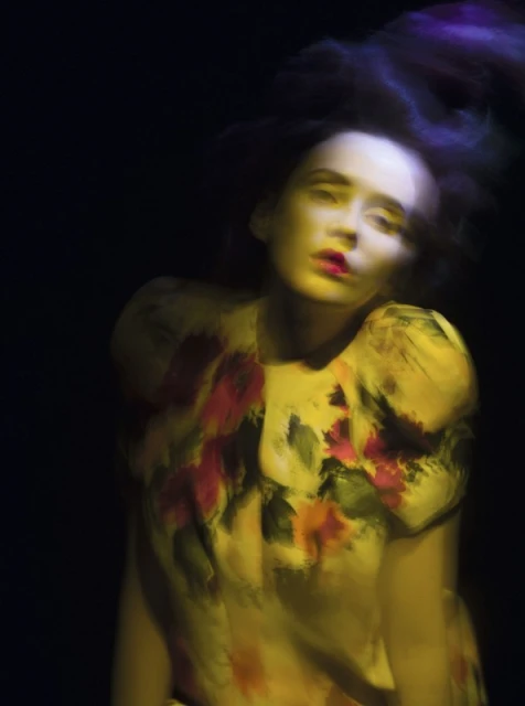 Woman in yellow floral dress with smeared colors and motion blur against a dark background in a fashion or beauty context.
