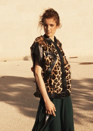 Woman wearing a leopard print vest and dark green skirt outdoors against a light stone wall by photographer Sarra Na.