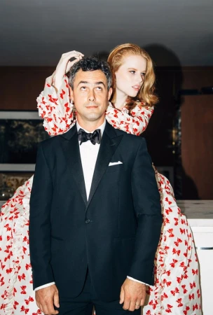 Man in black tuxedo standing with a red haired woman wearing a patterned dress styling his hair in Los Angeles
