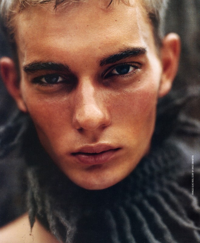 Close-up portrait of a fair-skinned young adult male with blond hair, wearing a grey woven scarf, captured in a beauty fashion style.