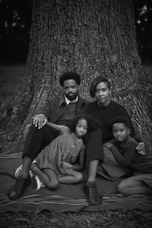 Monochrome portrait of a family of four sitting in front of a large tree outdoors. The family consists of parents, daughter, and son.