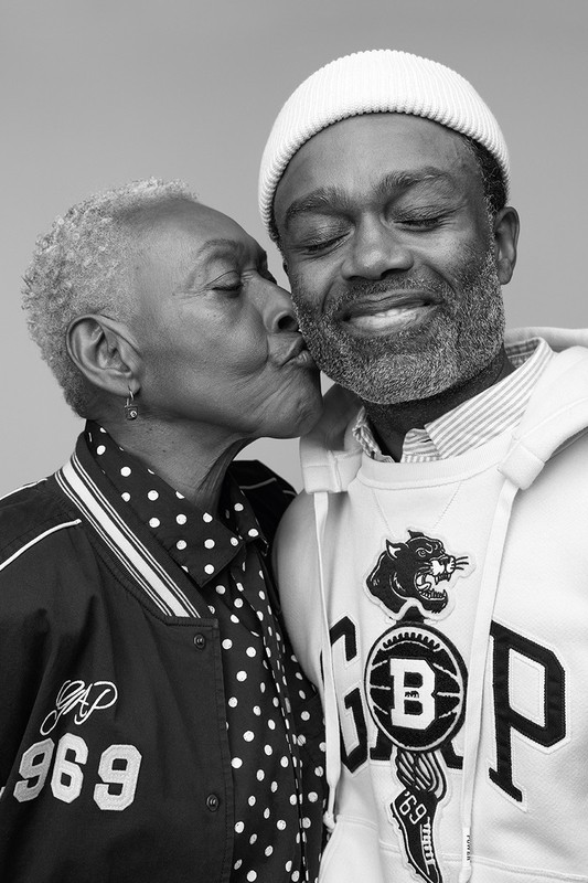 Black and white portrait of an older African American woman kissing a smiling African American man on the cheek in a studio setting.