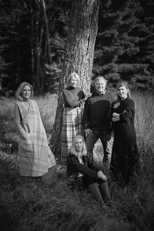 Group of five people posed outdoors in a grassy field beside a large tree in black and white photography.
