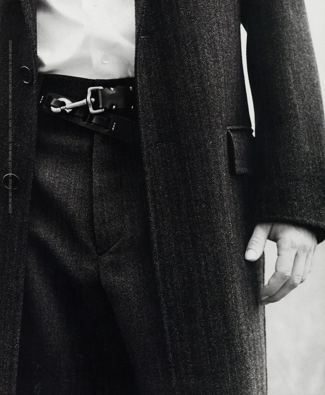 Close-up shot of a person wearing a herringbone coat, trousers, and a leather belt with a metal clasp, highlighting fashion and style.