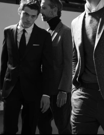 Black and white photograph of three adult males wearing formal suits and ties, posing indoors with a neutral background and bright lighting.