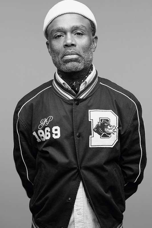 Black man wearing a beanie and a letterman jacket against a plain grey backdrop in Los Angeles.