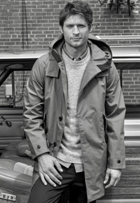 Man wearing hooded parka coat and knit sweater standing outdoors with a car and brick wall background