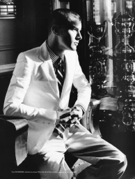 Black and white portrait of a man in a white suit and striped tie seated indoors by trophies