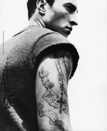 Monochrome portrait of a man in a textured knit sleeveless top showcasing arm tattoos styled by Scott Newkirk.