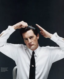 Man wearing white shirt and black tie combing his dark hair against dark background