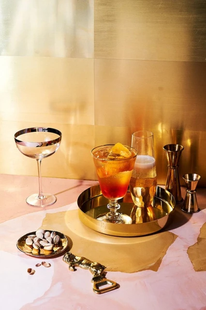 Cocktail glasses and bar tools on a colorful surface with a gold background, showcasing a mix of drinks and accessories for bar or home.