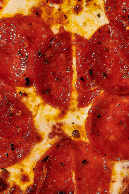 Macro shot of a pepperoni pizza with melted cheese, spices, and a crispy crust, capturing textures and vibrant red and yellow colors.