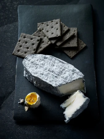 Overhead shot of a slate board with cheese, crackers, and an egg. The composition features cool tones and contrasts textures.