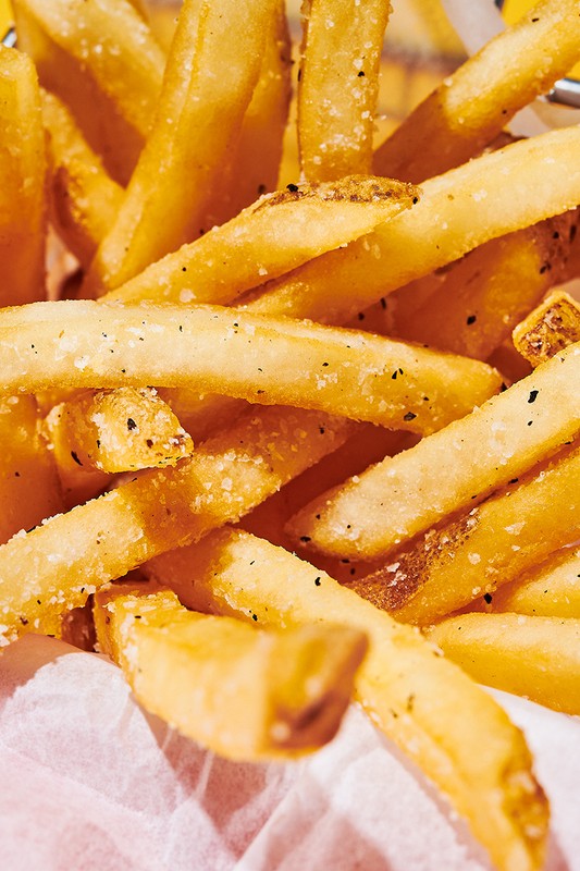 Close-up of a basket of golden, crispy French fries sprinkled with seasoning on white paper, ideal for food and fast-food visuals.