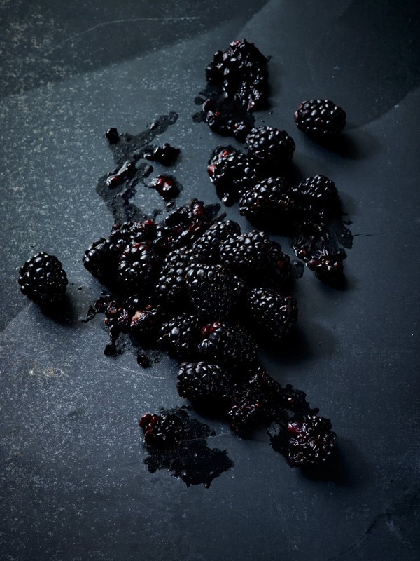 Overhead shot of fresh blackberries spread across a dark gray stone surface, some crushed, creating a rich, dark and textured composition.
