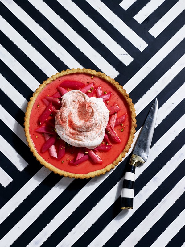 Overhead shot of a vibrant rhubarb tart topped with cream, placed on a striking black and white striped geometric background.