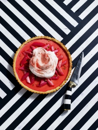 Overhead shot of a vibrant rhubarb tart topped with cream, placed on a striking black and white striped geometric background.