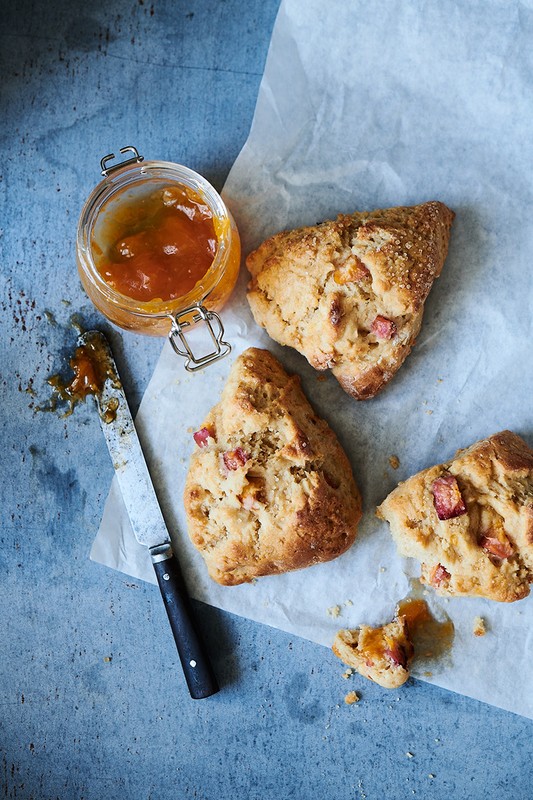 Overhead shot of scones with orange jam and a knife on parchment paper. Baked goods and jam make a rustic food presentation.