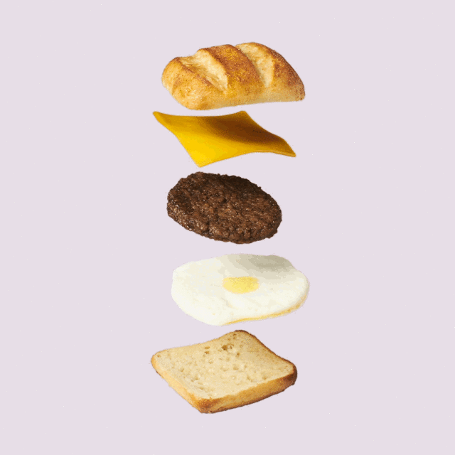 Overhead shot of an exploding sandwich: bread, cheese slice, meat patty, fried egg, and toast against a lavender background.
