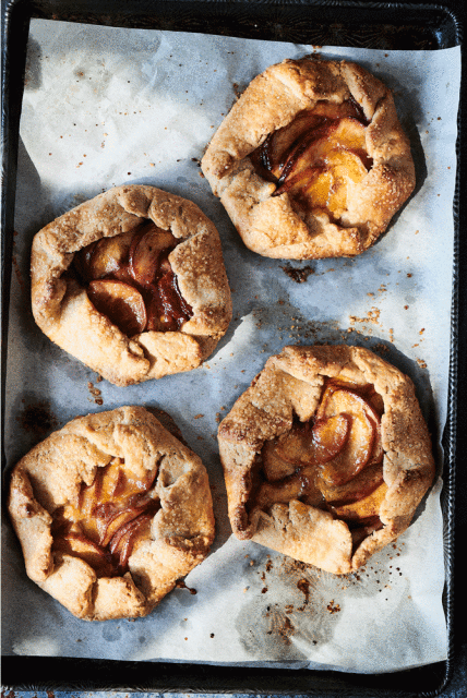 Overhead shot of four golden brown galettes with fruit filling on a parchment-lined baking sheet, creating a rustic and artisanal food presentation.