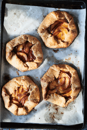 Overhead shot of four golden brown galettes with fruit filling on a parchment-lined baking sheet, creating a rustic and artisanal food presentation.
