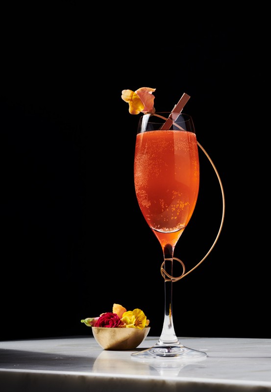 Elegant champagne flute filled with a sparkling orange cocktail, garnished with flowers and a chocolate stick, on a marble counter.