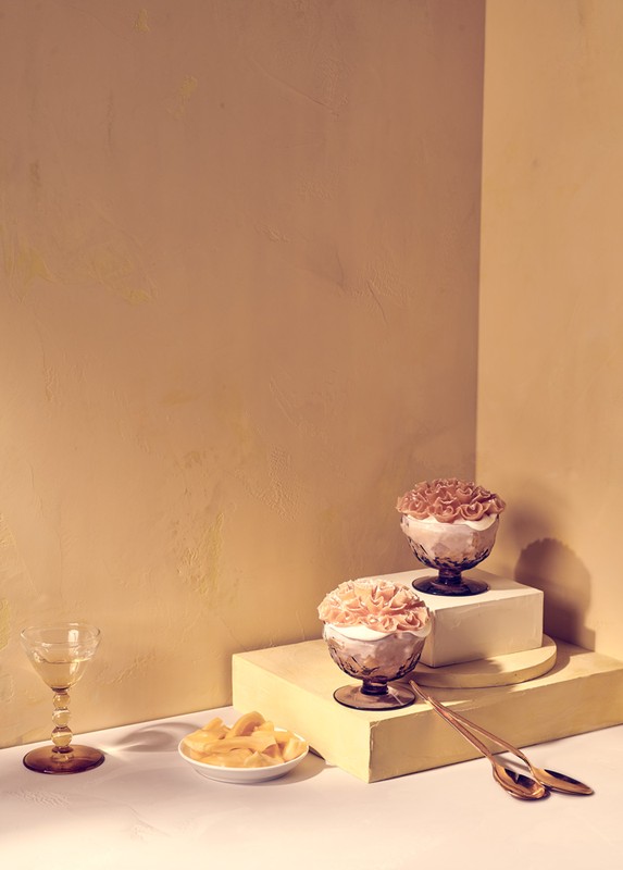Dessert still life: two ornate glass bowls with peach-colored dessert sit on platforms; plate of fruit and a wine glass are in the foreground.