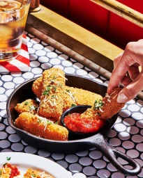 Hand dipping a golden fried mozzarella stick into marinara sauce in a cast iron skillet on a patterned tile table