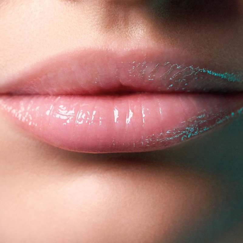 Close-up of a woman's shiny lips coated with pink lip gloss. Focus on beauty and makeup for a youthful and radiant look.