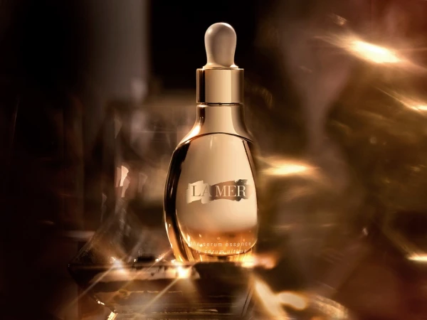 Close up product photography of a gold serum bottle with a dropper cap surrounded by warm glowing light flares.
