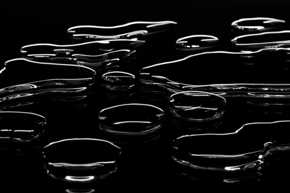 Abstract black background with reflective water droplets and surface ripples for use as wallpaper or graphic design asset.