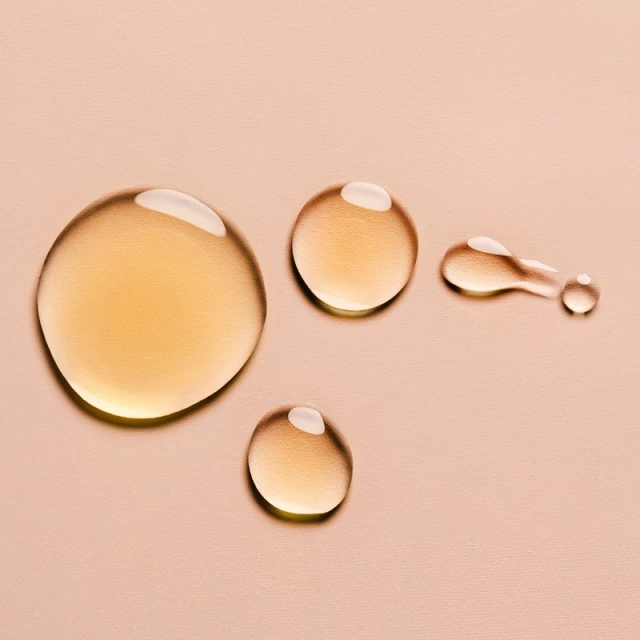 Close-up shot of golden liquid drops with a glossy finish on a neutral beige background, suitable for beauty or product imagery.