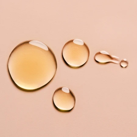 Close-up shot of golden liquid drops with a glossy finish on a neutral beige background, suitable for beauty or product imagery.