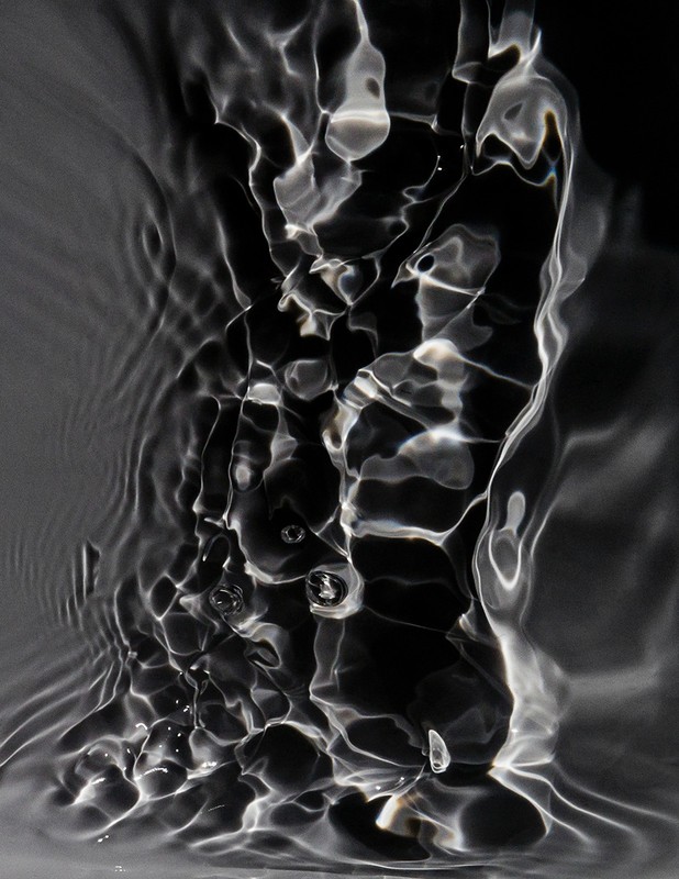 Abstract monochromatic image of rippling water with a black backdrop, creating an interplay of light and shadow in a fluid, dynamic composition.