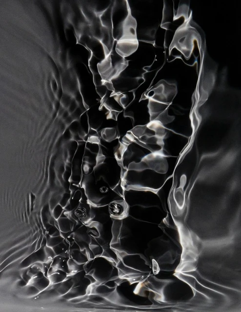 Abstract monochromatic image of rippling water with a black backdrop, creating an interplay of light and shadow in a fluid, dynamic composition.