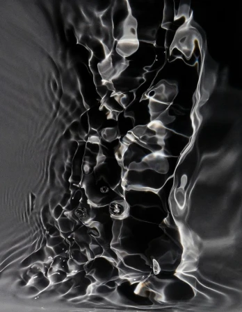 Abstract monochromatic image of rippling water with a black backdrop, creating an interplay of light and shadow in a fluid, dynamic composition.