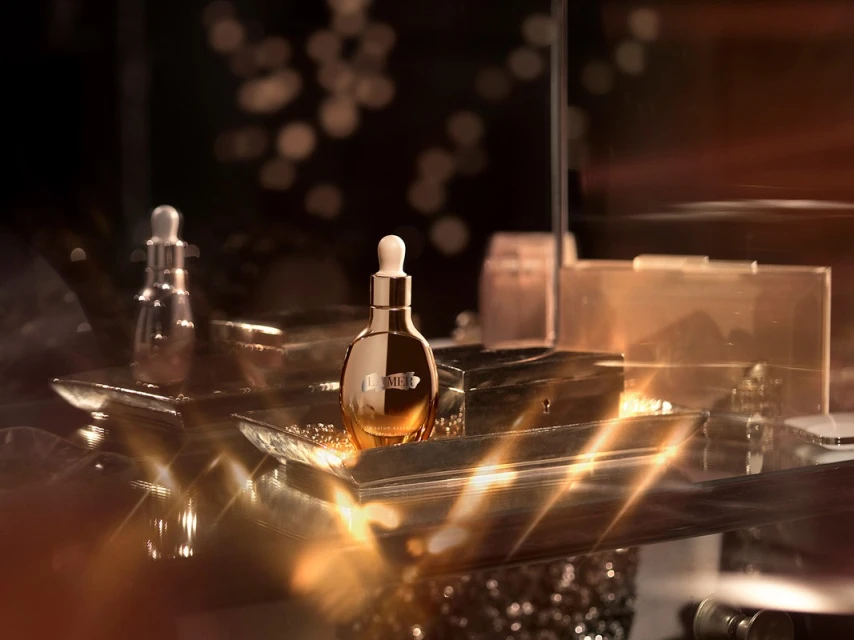 La Mer skincare product bottles displayed on a reflective surface with bokeh lights in the background. Beauty and luxury concept.