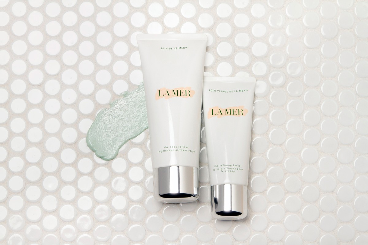 Close-up of La Mer skincare products against a bright white mosaic tile background, highlighting the brand's body and face refiner creams.