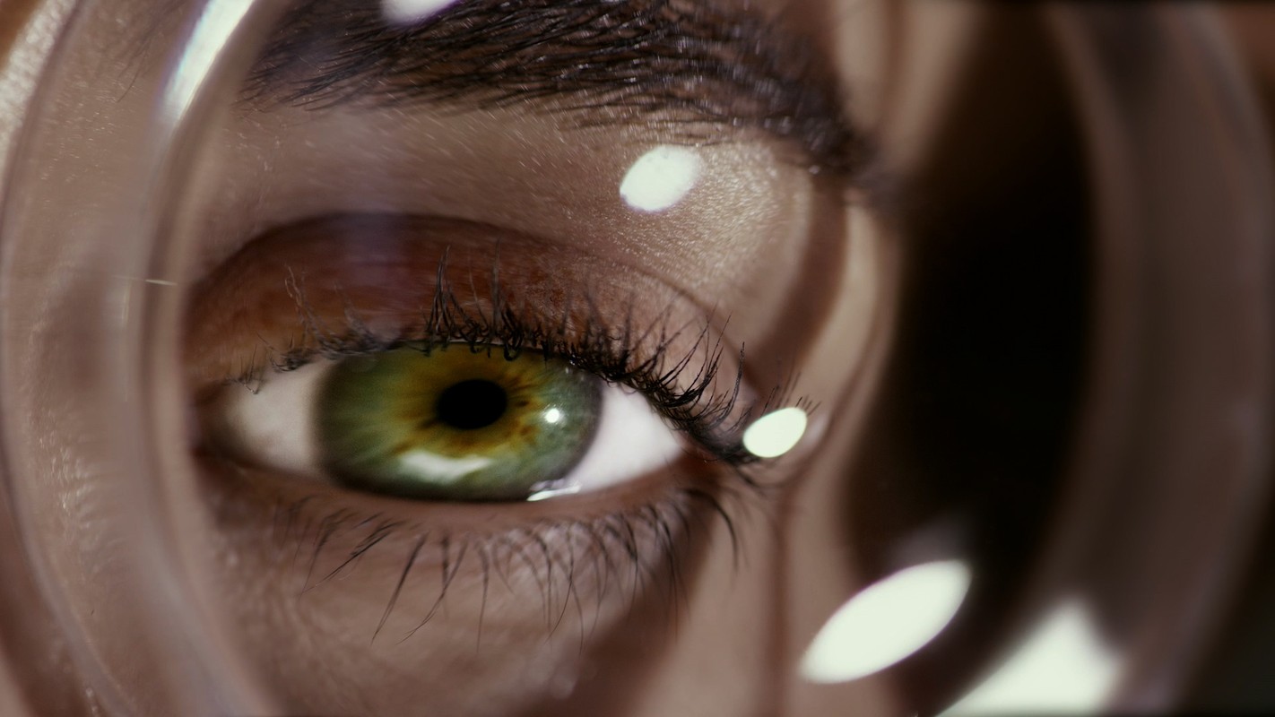 Extreme close-up of a green eye with long eyelashes, captured through a clear lens, highlighting texture and vibrant color.