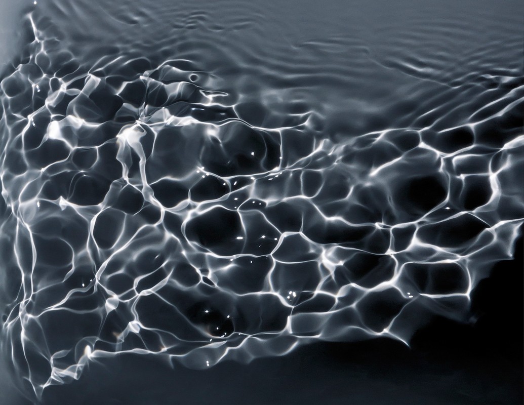 Monochromatic water surface ripples with abstract patterns of light and shadow create a mesmerizing, rippled texture in this close-up shot.