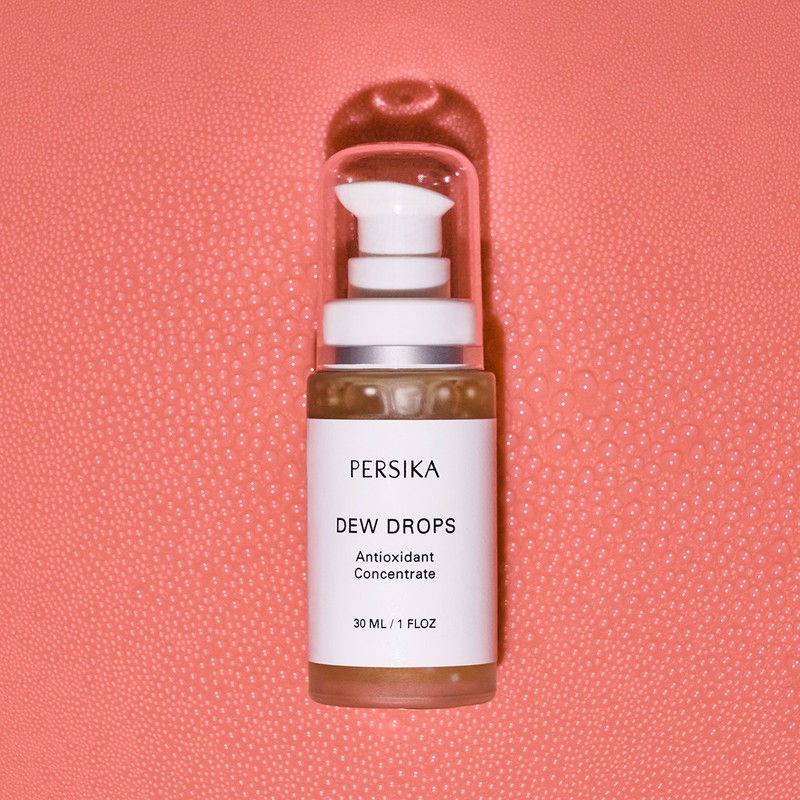 Persika Dew Drops antioxidant concentrate bottle on a textured coral backdrop, product shot with minimalist presentation.