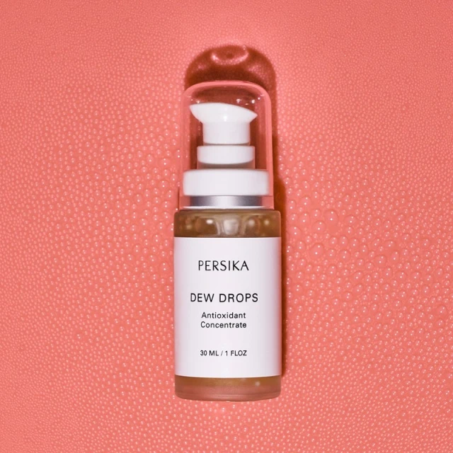Persika Dew Drops antioxidant concentrate bottle on a textured coral backdrop, product shot with minimalist presentation.