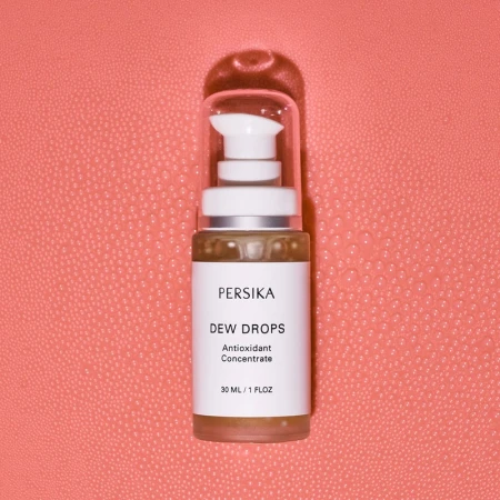 Persika Dew Drops antioxidant concentrate bottle on a textured coral backdrop, product shot with minimalist presentation.