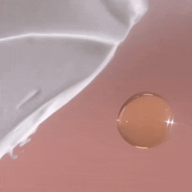 Close-up studio shot of a white lotion swirl alongside a transparent golden oil droplet on a pink background, showcasing texture.