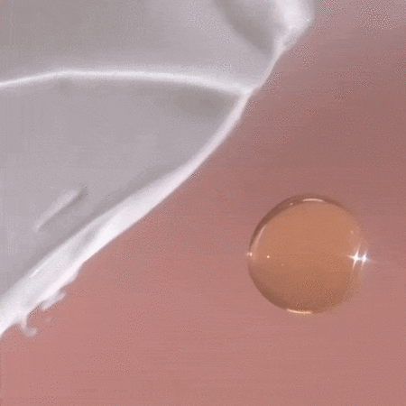 Close-up studio shot of a white lotion swirl alongside a transparent golden oil droplet on a pink background, showcasing texture.