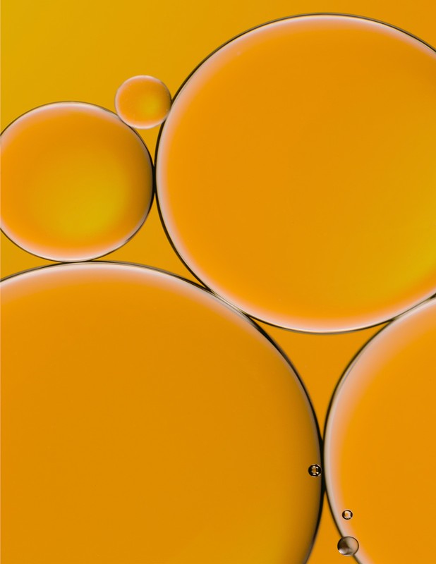 Abstract shot of orange liquid containing oil droplets in varying sizes and translucent amber colors against a bright background.