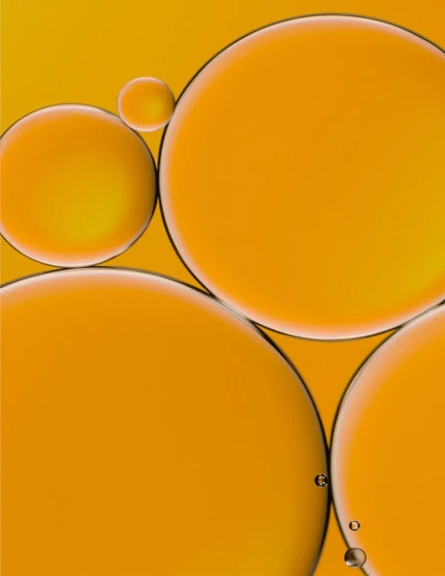 Abstract shot of orange liquid containing oil droplets in varying sizes and translucent amber colors against a bright background.