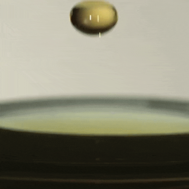 Macro shot of a golden liquid drop suspended above a dark, glossy surface, creating a captivating moment frozen in time.