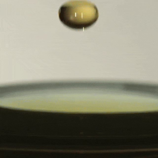 Macro shot of a golden liquid drop suspended above a dark, glossy surface, creating a captivating moment frozen in time.